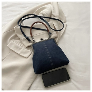 Detail of blue denim crossbody bag with brown leather handle and metal clasp closure