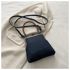 Close-up of retro denim kiss-lock crossbody bag on beige blazer with leather handles