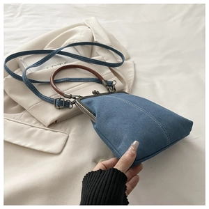 Detail of dark blue denim crossbody bag featuring vintage metal clasp and leather handle