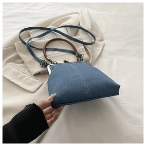 Close-up of vintage denim mini bag with metal clasp and brown leather handle on blazer
