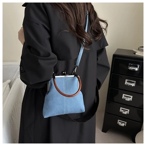 Model showing a light blue denim kiss-lock crossbody bag with a brown circular handle