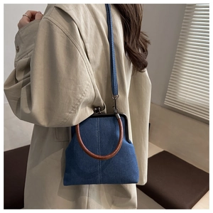 Detail of blue denim crossbody bag with metal clasp and brown round handle on a model