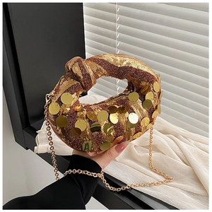 Detailed macro view of golden sequin handbag with knot handle and gold chain strap