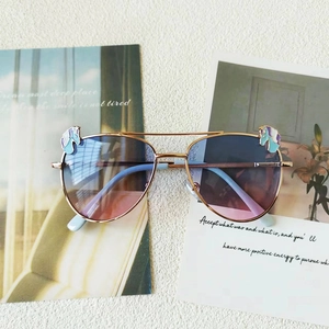Détail de lunettes pilote avec monture dorée, motif licorne et verres dégradés rose-bleu