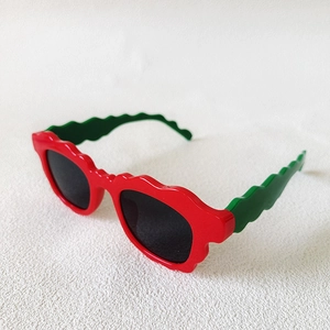 Détail de lunettes de soleil ondulées avec cadre rouge et vert et verres sombres