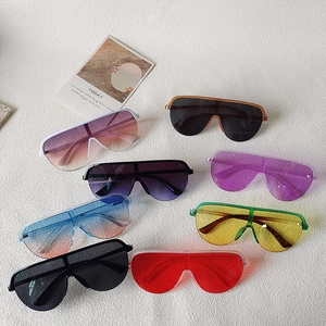 Flat lay display of multi-colored oversized wrap-around sunglasses on textured fabric