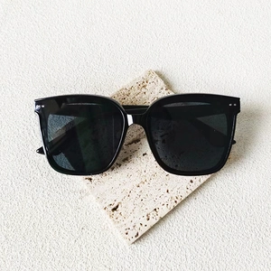 Lunettes de soleil carrées noires avec rivets argentés sur plateforme en pierre