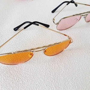Dettaglio di occhiali da sole aviator arancioni e rosa con montature in metallo dorato