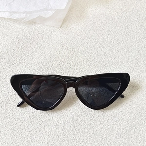 Top-down view of black vintage cat-eye sunglasses with dark grey UV lenses on white textured background