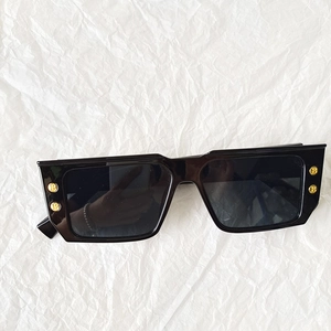 Detail of black rectangular sunglasses featuring golden B-logo metal studs on the frame