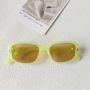 Détail de lunettes de soleil carrées vert néon avec rivets sur fond texturé blanc