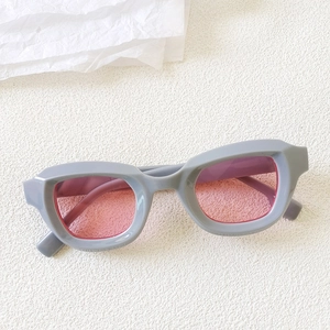 Detail of grey bubble frame cat eye sunglasses with transparent pink lenses on white texture