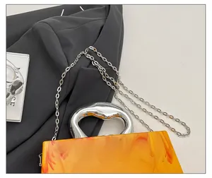 Close-up of amber acrylic evening bag featuring a unique silver metallic handle and chain