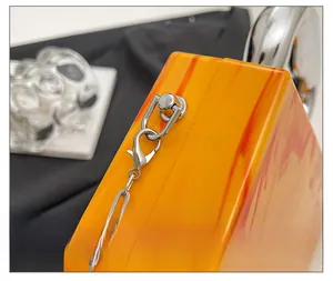 Macro shot of silver hardware and metal chain on orange marble acrylic evening clutch