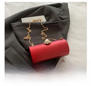 Sac de soirée cylindrique rouge avec fermoir perle et chaîne à côté d'un smartphone