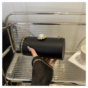 Détail de la pochette cylindrique noire avec fermoir perle et bandoulière chaîne dorée