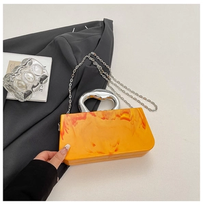 Orange marble acrylic clutch with silver sculptural handle on a dark grey blazer