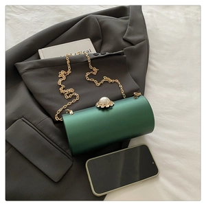 Détail du sac cylindrique vert foncé avec chaîne dorée et fermoir perle sur une veste