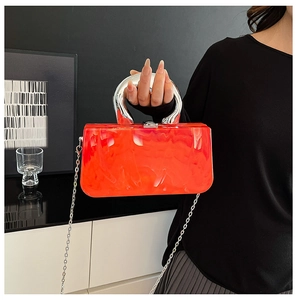 Detailed macro view of orange acrylic clutch bag with marble texture and silver metal handle