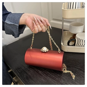 Détail du sac de soirée cylindrique rouge avec finition soie, fermoir perle et chaîne dorée