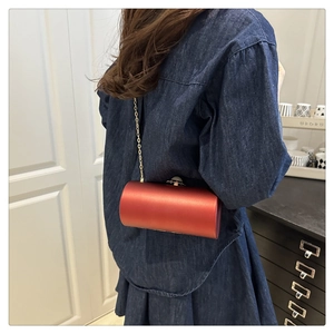 Détail du sac de soirée cylindrique rouge avec chaîne dorée et fermoir perle sur modèle
