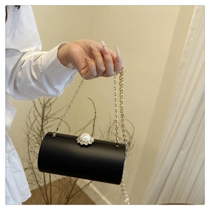Détail d'une pochette cylindrique noire avec fermoir perle et bandoulière dorée