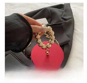 Detalle de bolso de noche circular rojo con asa de cuentas doradas y cadena de metal