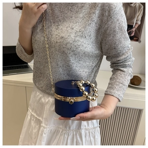 Detalle de bolso de noche acrílico azul oscuro con asa de perlas doradas y cadena metálica