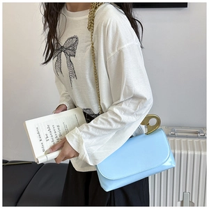Sac à bandoulière bleu clair avec chaîne dorée posé à côté d'une valise blanche