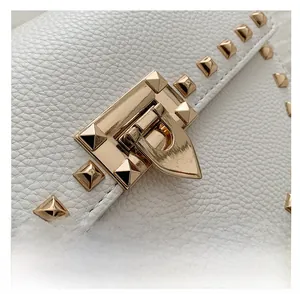 Detailed close-up of white lychee leather texture and golden square rivets on handbag
