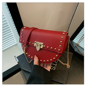 Detail of red pebbled leather saddle bag with golden pyramid studs and chain strap