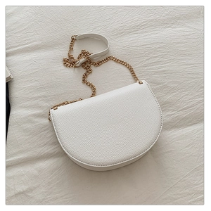 Close-up of white lychee grain leather saddle bag with golden chain strap on fabric
