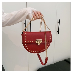 Detail of red pebbled leather saddle bag with gold square studs and chain strap