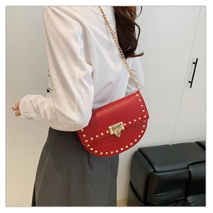 Detail view of red pebbled leather saddle bag featuring gold rivets and chain strap