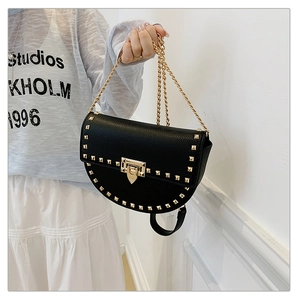 Detail of black saddle bag featuring gold studs, leather texture, and chain strap