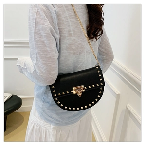 Detail of black saddle bag with golden studs and metal chain strap on model