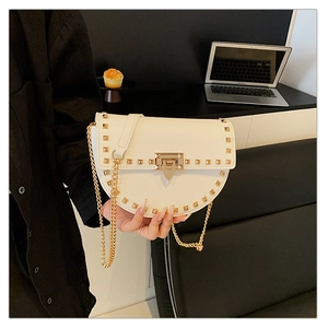 Detail of off-white saddle bag with gold studs and chain strap in a lifestyle setting