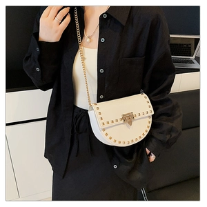 Detail of cream saddle bag with gold studs and chain strap on a black shirt
