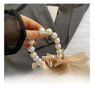 Detail of champagne satin bucket bag with pearl handle and silk bow decoration