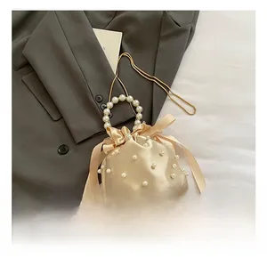 Detail of champagne satin bucket bag with pearl handle and golden chain strap
