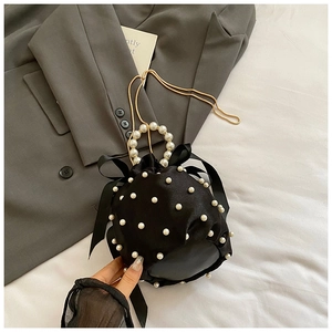 Detail of black satin bucket bag featuring pearl handle and silk ribbon bow accents