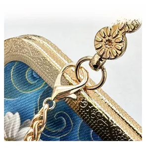 Macro shot of gold metal frame with floral carving and chain link on a blue embroidered bag
