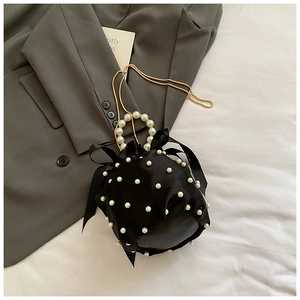 Detail of black satin bucket bag with white pearls, silk bow and gold snake chain strap