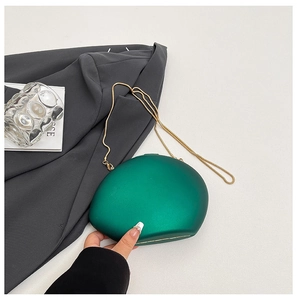 Macro view of dark green hard shell egg-shaped clutch bag with golden chain detail