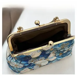 Detail display of butterfly embroidery on vintage shell bag with gold kiss-lock closure