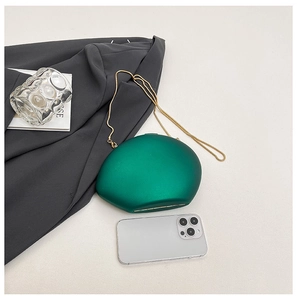 Deep green pebble-shaped acrylic clutch bag with a delicate gold chain strap on a desk
