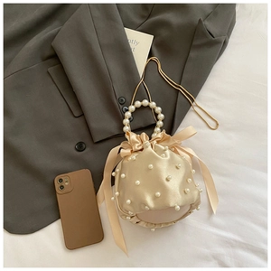 Macro detail of champagne silk bucket bag with pearl handle and bow decoration