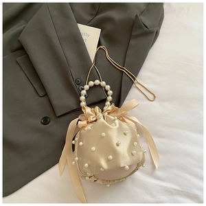 Detailed close-up of champagne satin bucket bag with pearl handle and bow drawstring