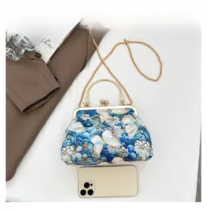 Detail view of mini butterfly embroidery shell bag with metal chain beside a phone for scale