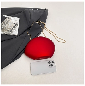 Macro detail of red matte clutch bag with gold chain next to a smartphone for size scale